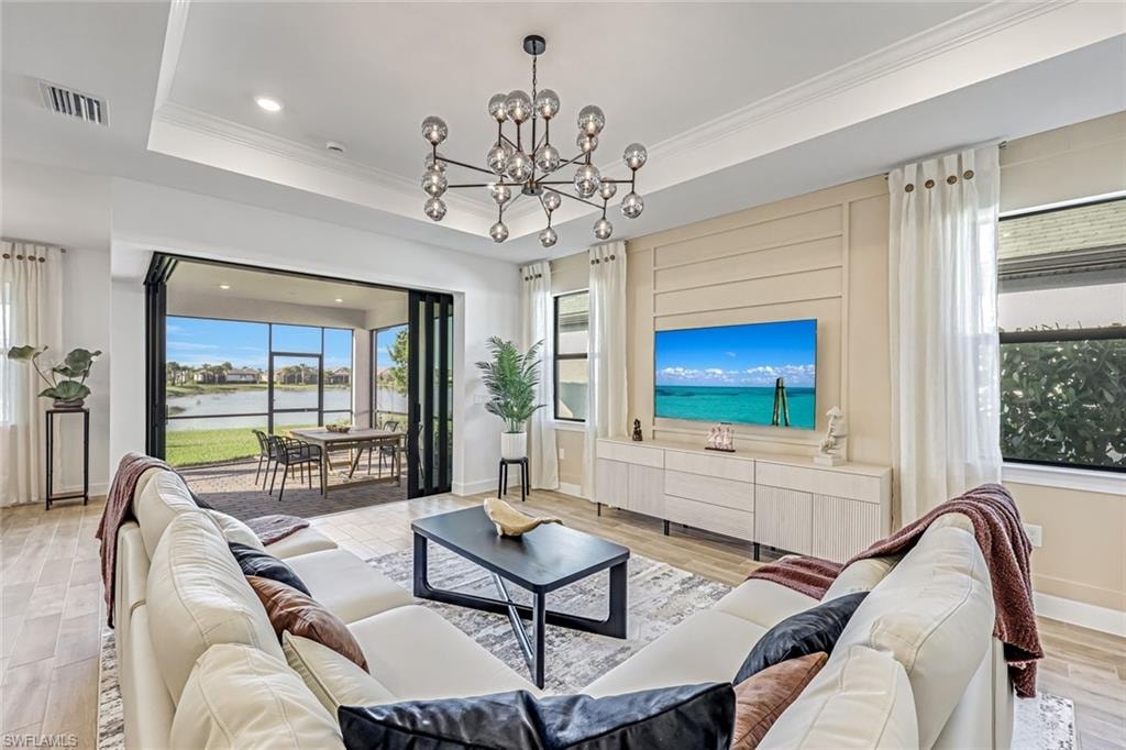 Living area featuring light wood-style floors, ornamental molding, recessed lighting, a chandelier, and a tray ceiling