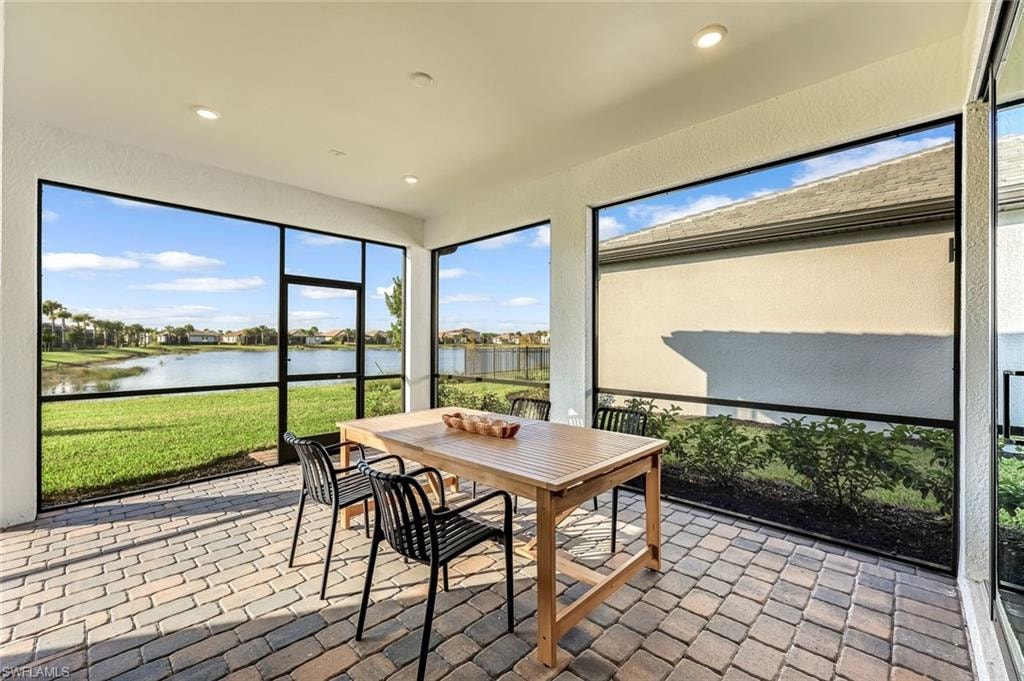Sunroom with outdoor dining area, a water view, a textured wall, recessed lighting, and a patio