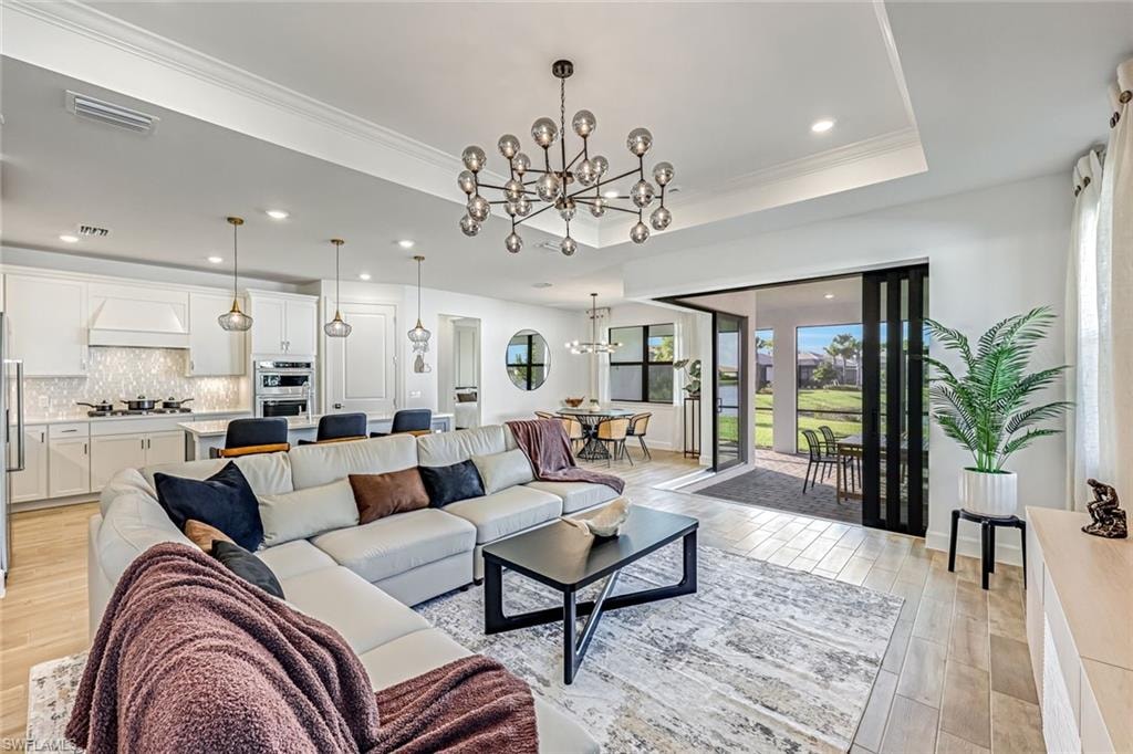 Living room with a chandelier, light wood-style flooring, recessed lighting, and crown molding