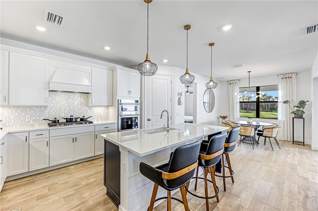 Kitchen with hanging light fixtures, light wood-style flooring, white cabinets, and recessed lighting