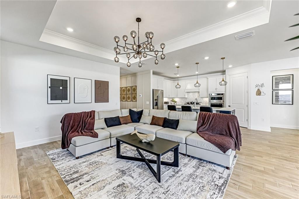 Living room with a chandelier, ornamental molding, recessed lighting, light wood finished floors, and a tray ceiling