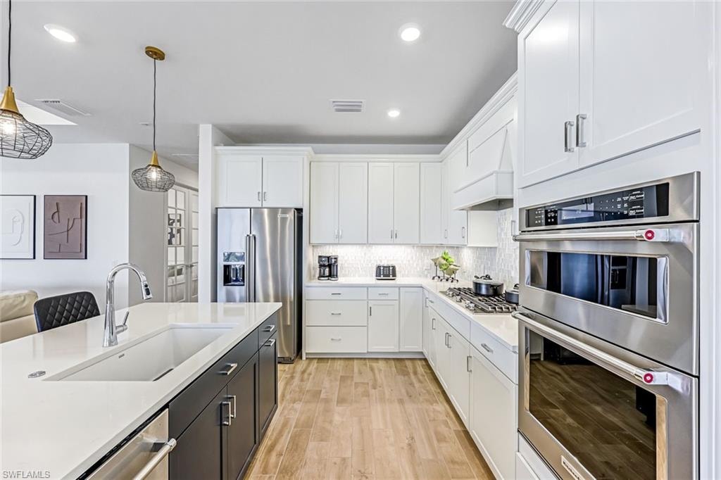 Kitchen with stainless steel appliances, white cabinetry, pendant lighting, light stone countertops, and custom range hood
