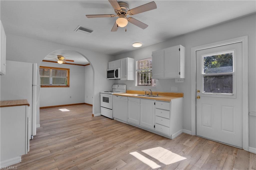 Kitchen featuring a ceiling fan, white appliances, white cabinets, light countertops, and light wood-style flooring