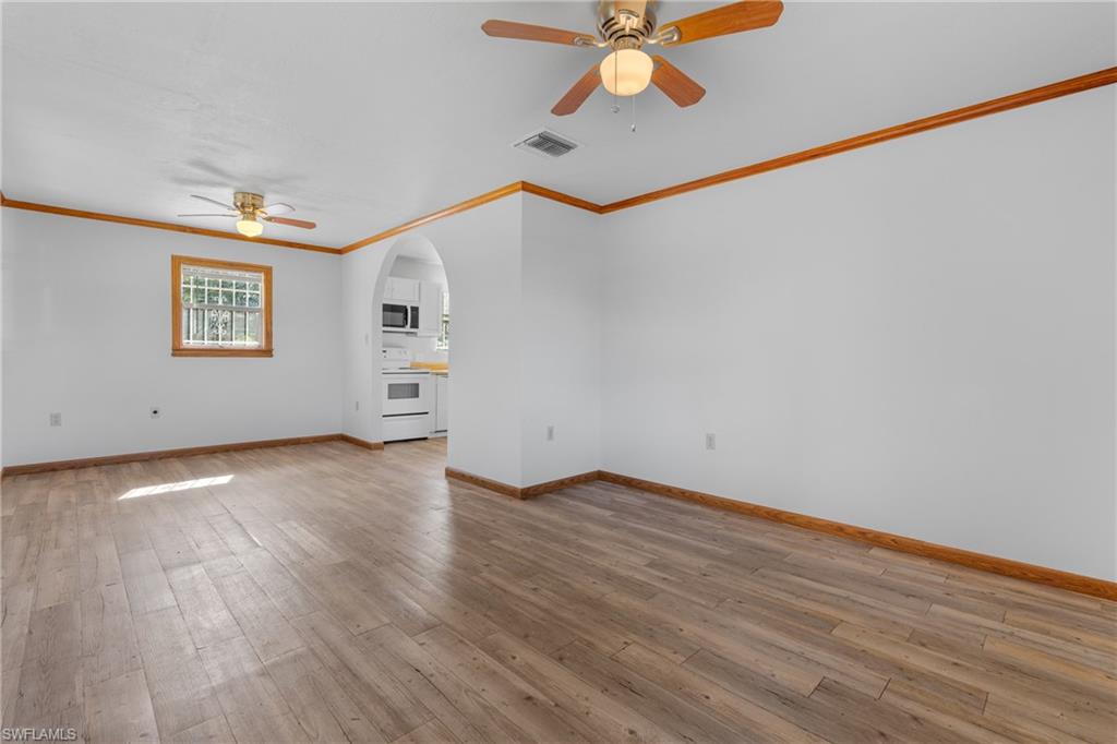 Unfurnished living room with ceiling fan, light wood-style floors, arched walkways, and crown molding