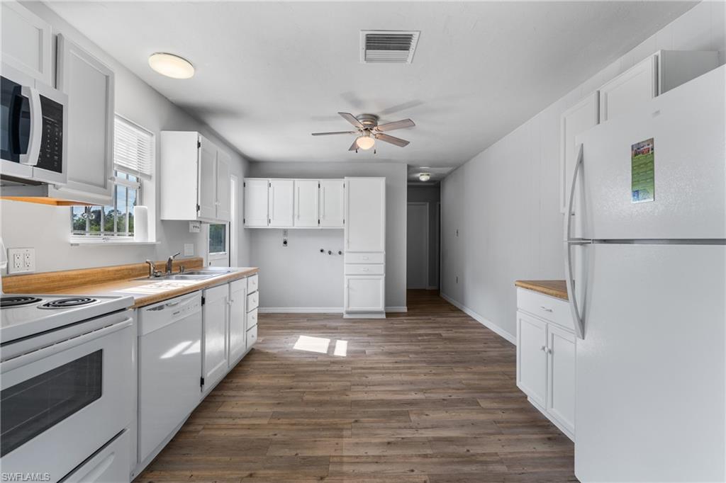 Kitchen featuring white appliances, white cabinets, dark wood finished floors, and a ceiling fan