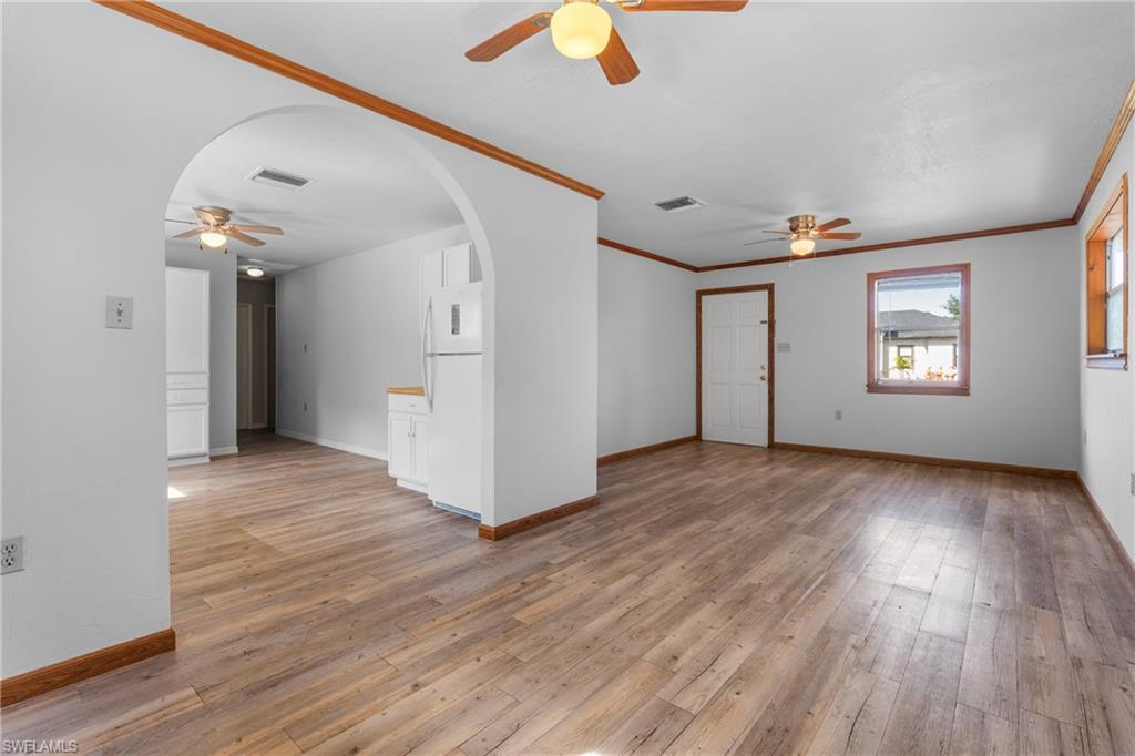 Unfurnished living room with ceiling fan, arched walkways, ornamental molding, and light wood finished floors