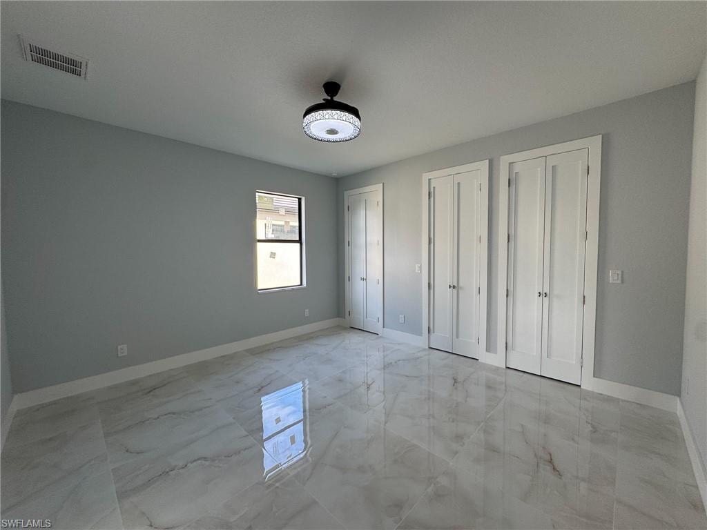 Unfurnished bedroom featuring multiple closets and light marble finish floors
