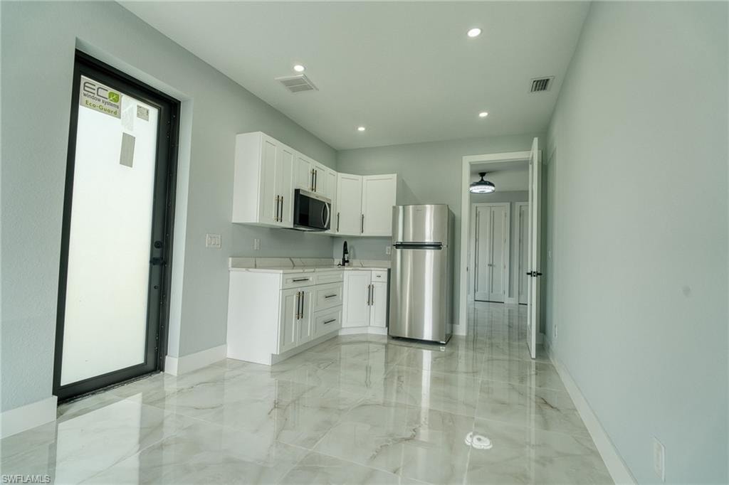Kitchen featuring white cabinets, appliances with stainless steel finishes, light marble finish flooring, recessed lighting, and light stone counters