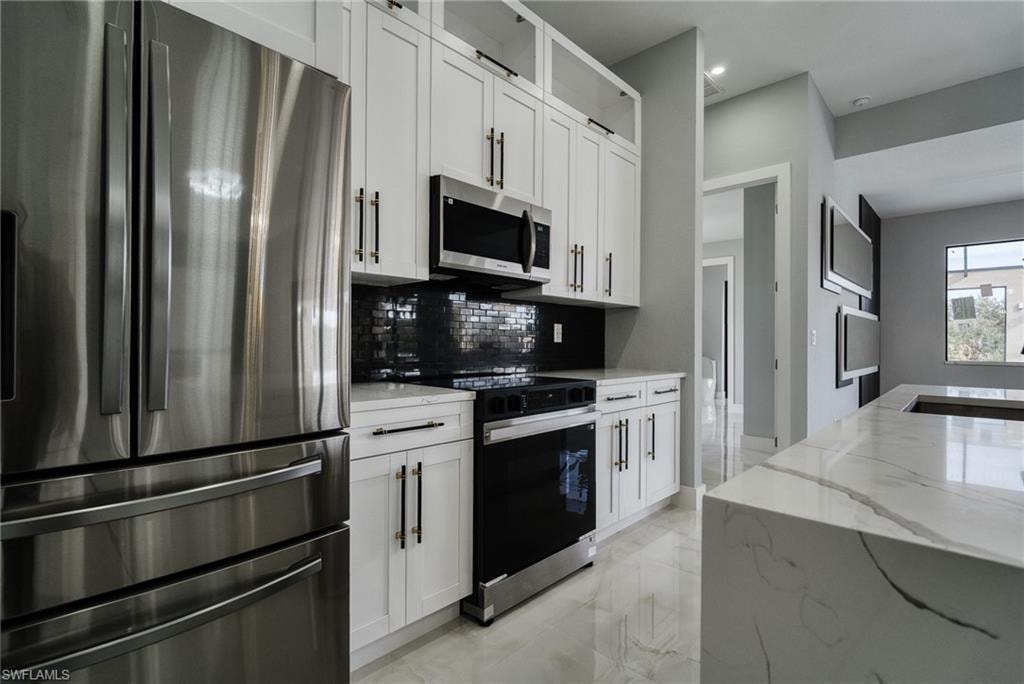 Kitchen featuring appliances with stainless steel finishes, light stone countertops, and white cabinetry