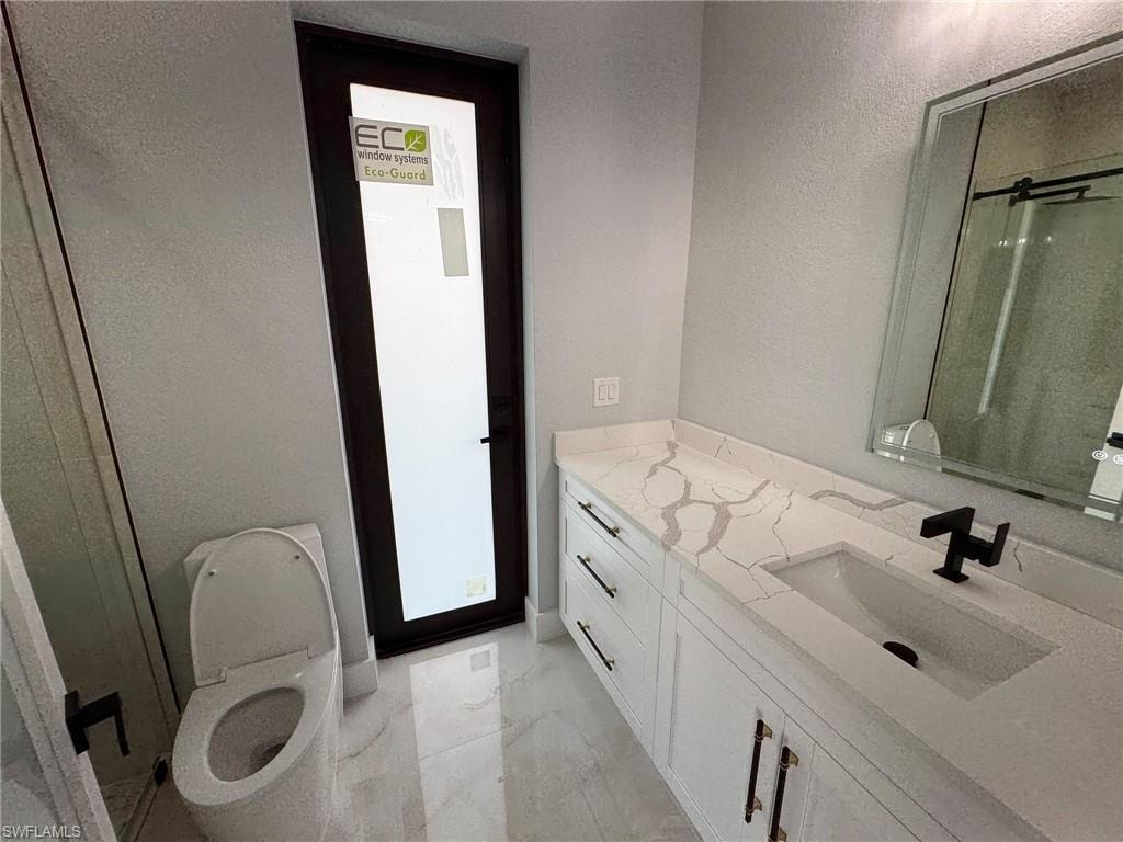 Bathroom with a stall shower, vanity, a textured wall, and light marble finish flooring