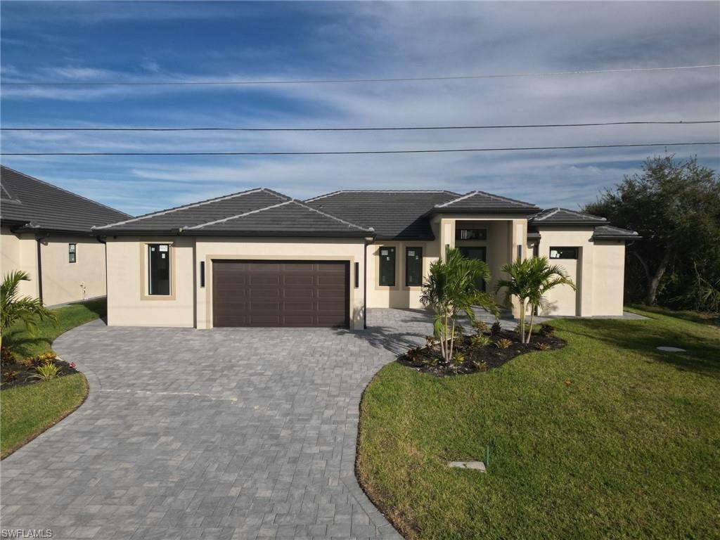 Prairie-style home featuring stucco siding, a front yard, an attached garage, decorative driveway, and a tiled roof