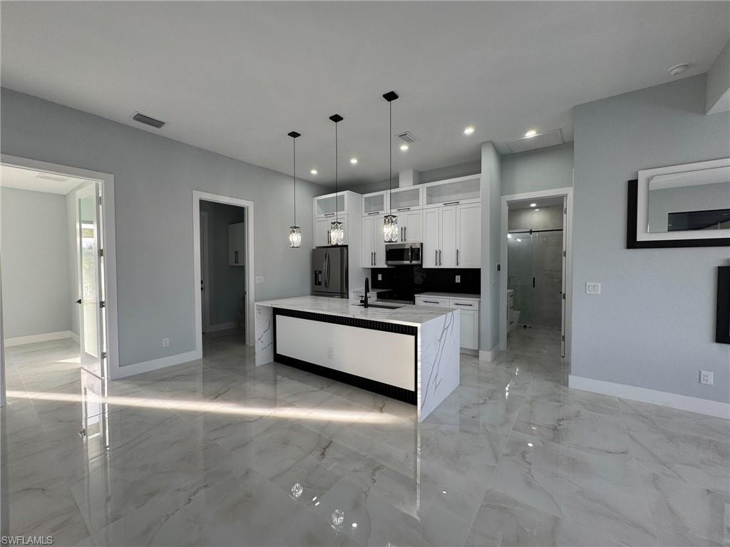 Kitchen featuring white cabinetry, light stone counters, hanging light fixtures, appliances with stainless steel finishes, and light marble finish flooring
