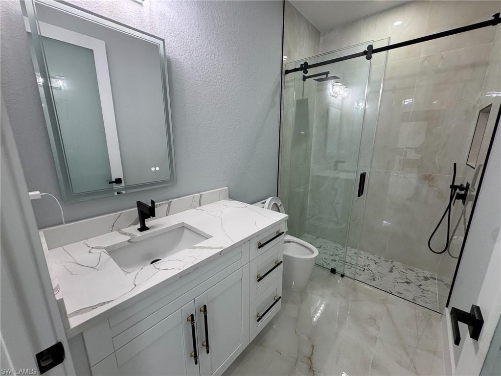 Bathroom featuring vanity, a textured wall, a shower stall, and light marble finish floors