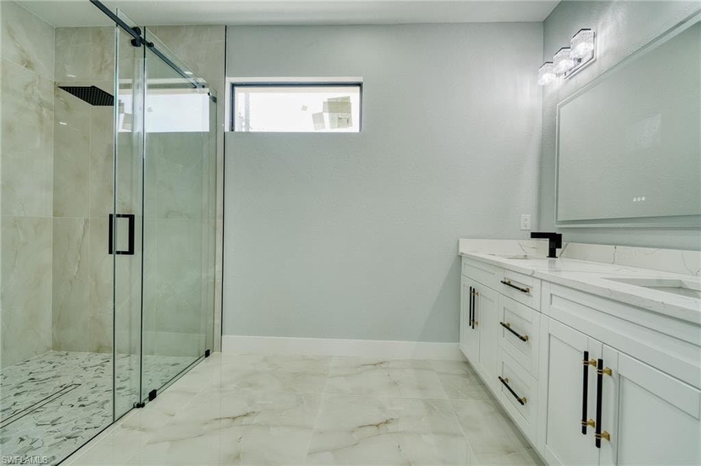 Full bathroom featuring double vanity, a marble finish shower, and light marble finish floors
