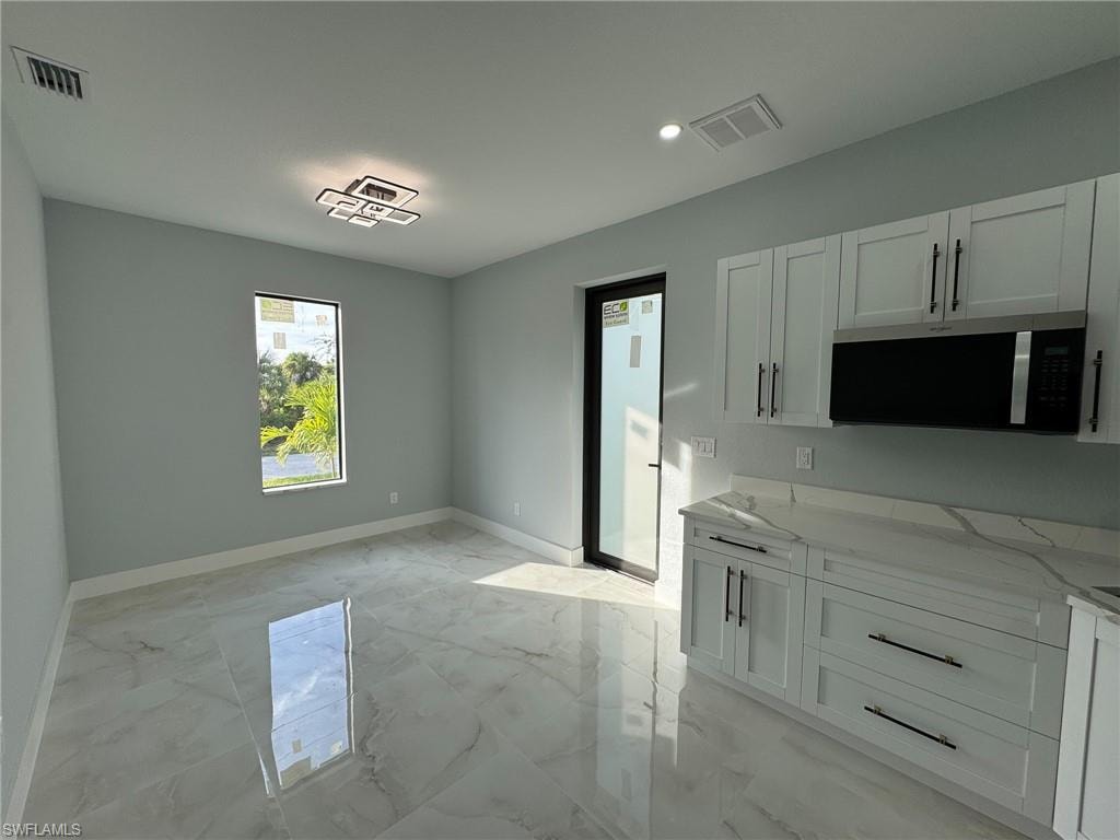 Kitchen featuring light stone countertops, white cabinets, stainless steel microwave, light marble finish floors, and recessed lighting