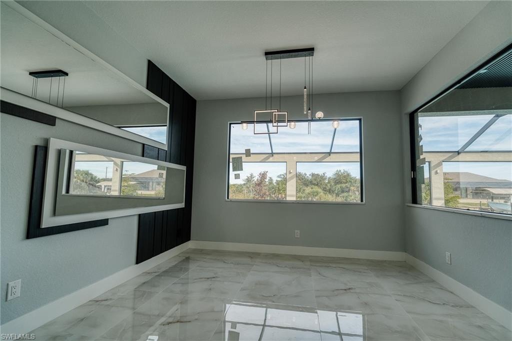 Unfurnished dining area featuring light marble finish floors, plenty of natural light, and a chandelier