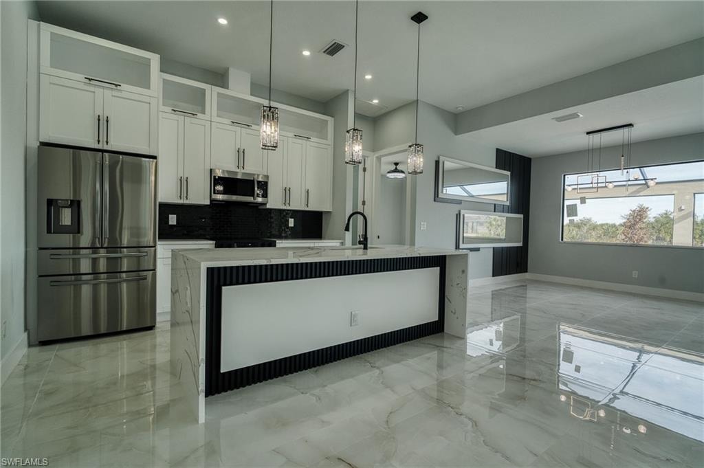 Kitchen featuring appliances with stainless steel finishes, pendant lighting, light stone countertops, a center island with sink, and decorative backsplash
