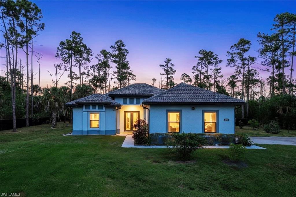 Back of property at dusk featuring a lawn, a tile roof, and stucco siding