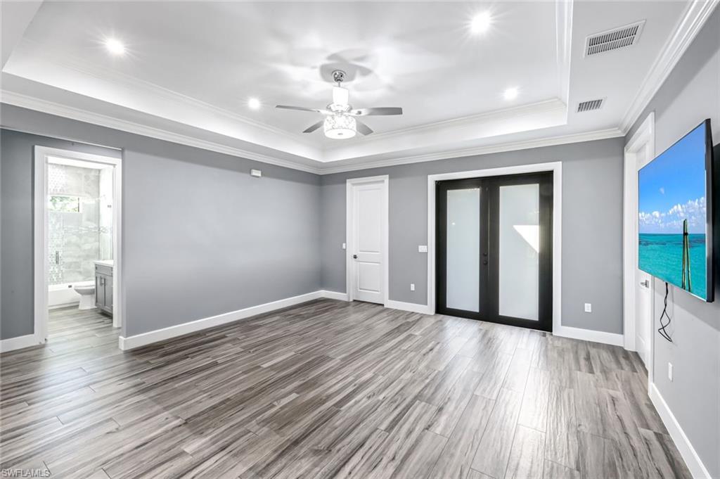 Unfurnished bedroom with french doors, a raised ceiling, ceiling fan, light wood-style flooring, and crown molding