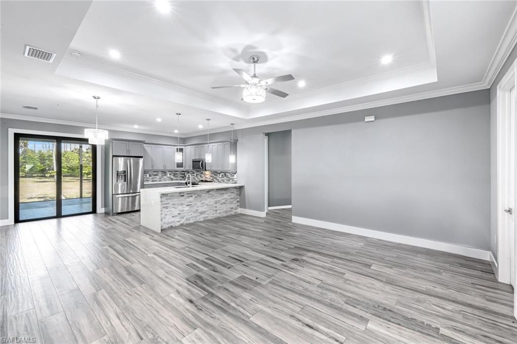Kitchen featuring open floor plan, stainless steel appliances, a ceiling fan, ornamental molding, and gray cabinets