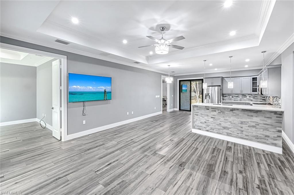 Unfurnished living room featuring ornamental molding, a ceiling fan, recessed lighting, a tray ceiling, and light wood-style flooring