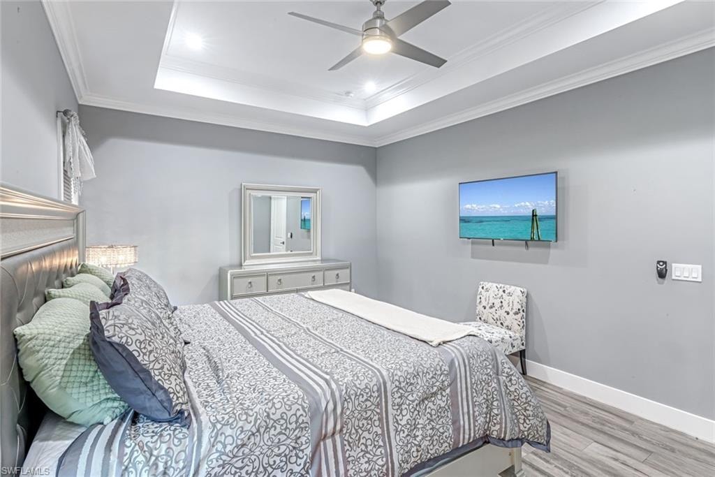 Bedroom with ornamental molding, light wood-type flooring, ceiling fan, and a raised ceiling