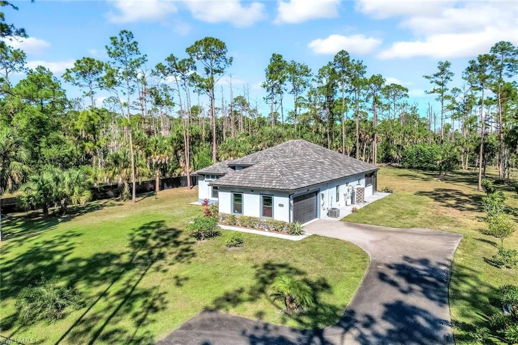 View of front of property featuring a front lawn, stucco siding, driveway, an attached garage, and view of scattered trees