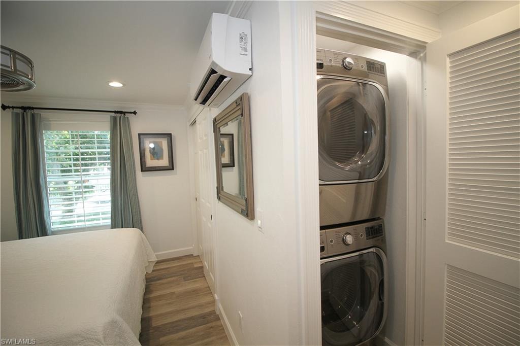 Laundry area with ornamental molding, stacked washer / dryer, an AC wall unit, dark wood-style floors, and recessed lighting