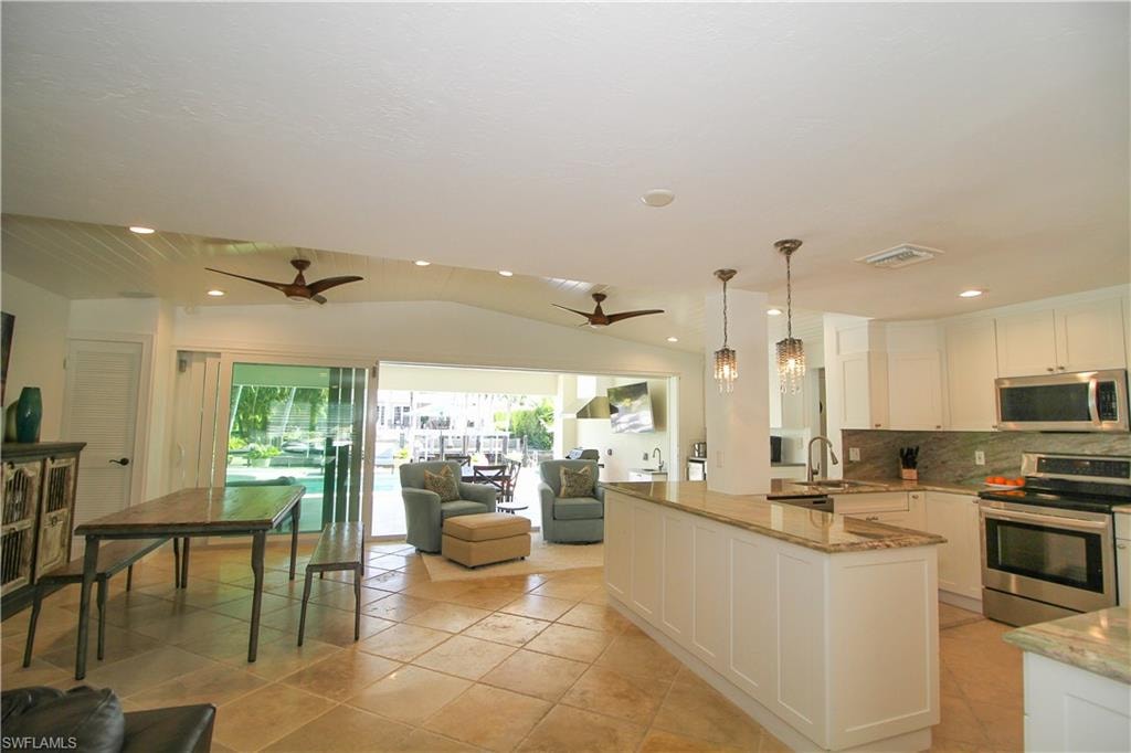 Kitchen with vaulted ceiling, stainless steel appliances, white cabinetry, light stone counters, and hanging light fixtures