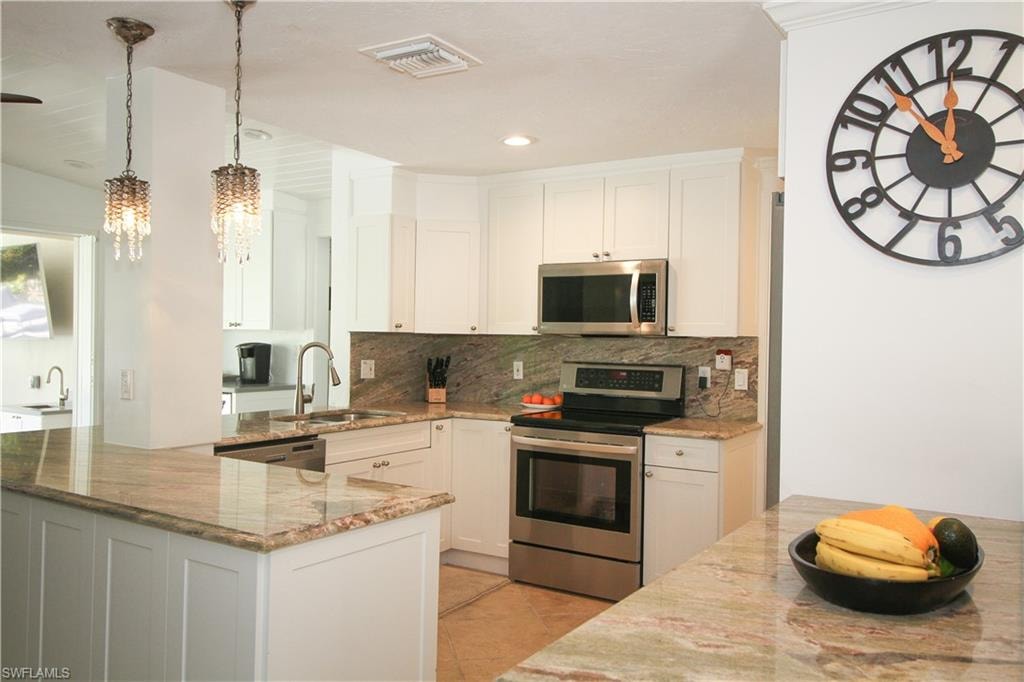 Kitchen with stainless steel appliances, white cabinets, light stone countertops, decorative light fixtures, and recessed lighting