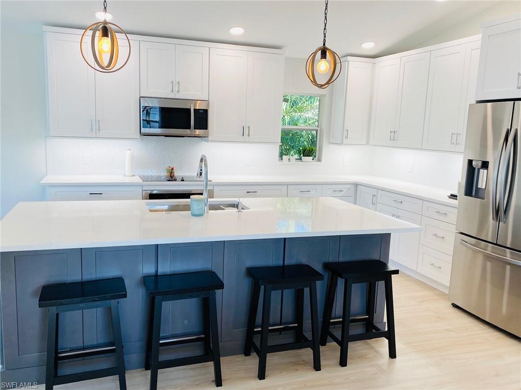 Kitchen with stainless steel appliances, white cabinets, pendant lighting, light wood-style floors, and a kitchen island with sink
