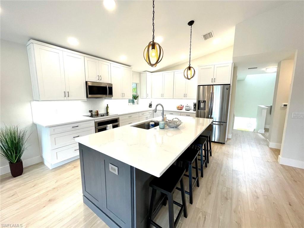 Kitchen with white cabinets, appliances with stainless steel finishes, a breakfast bar area, a kitchen island with sink, and decorative light fixtures