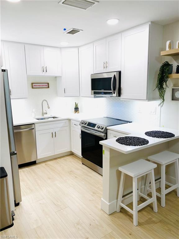 1st floor Kitchen with stainless steel appliances, a breakfast bar area, white cabinets, and decorative backsplash