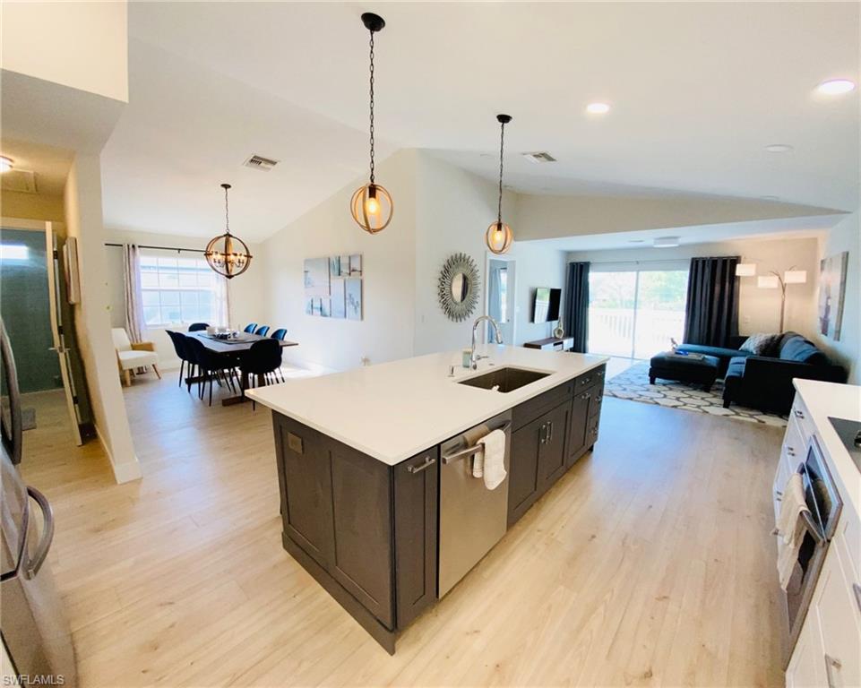 Kitchen with hanging light fixtures, open floor plan, healthy amount of natural light, light wood-style flooring, and high vaulted ceiling