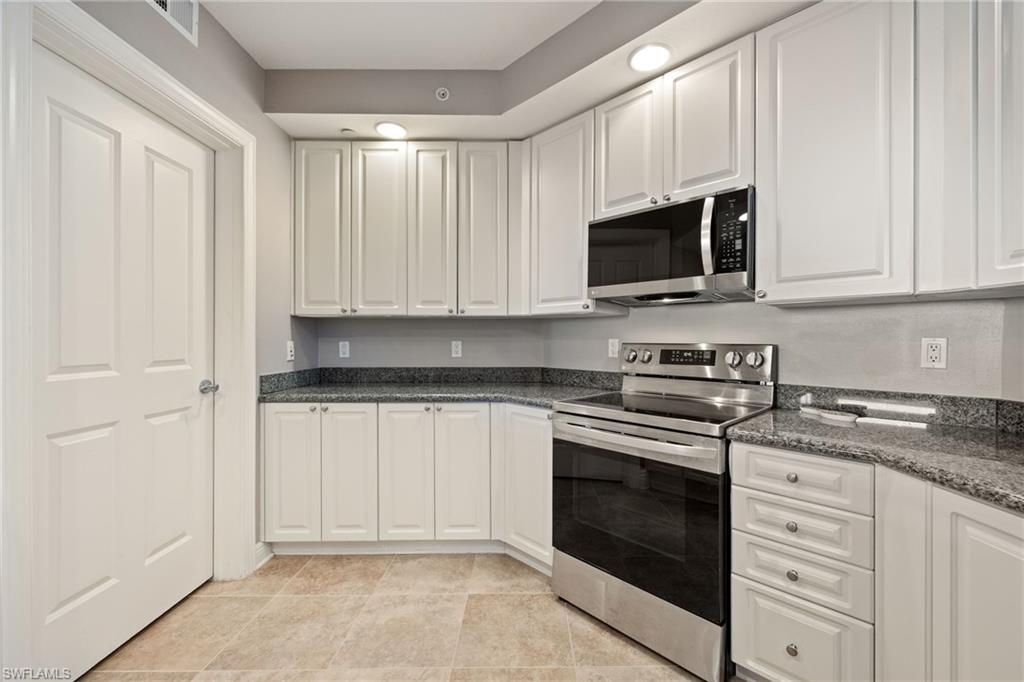 Kitchen with stainless steel appliances, white cabinets, and dark stone counters