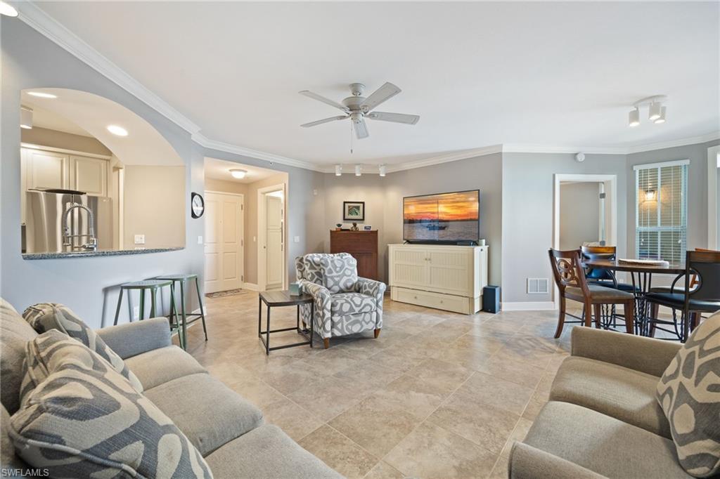 Living area with crown molding, arched walkways, and ceiling fan