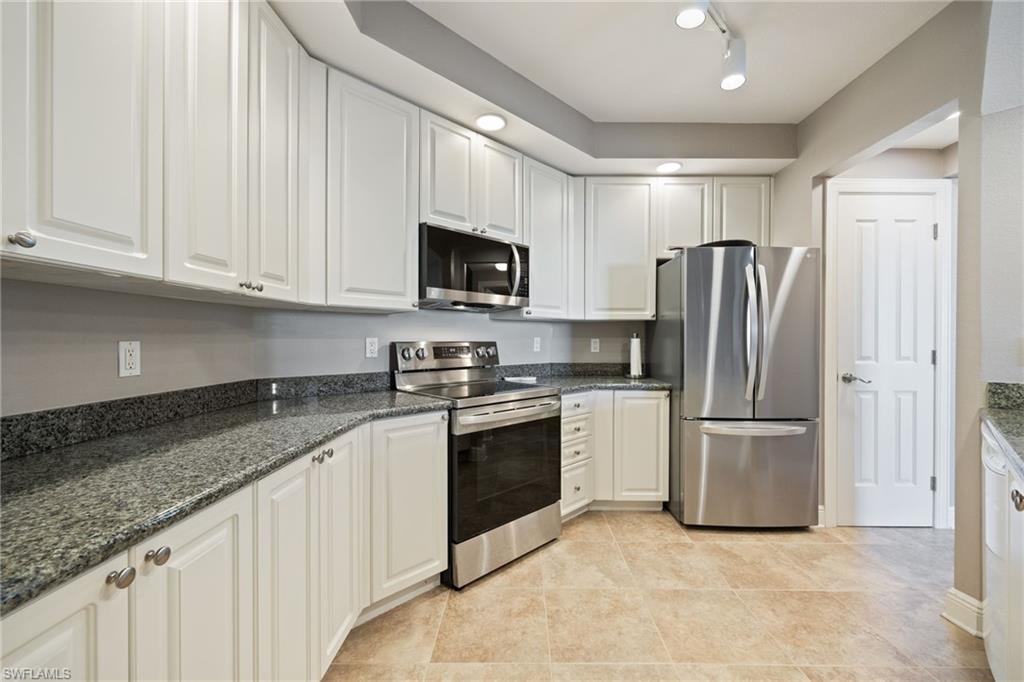 Kitchen with stainless steel appliances, white cabinets, dark stone counters, light tile patterned floors, and rail lighting