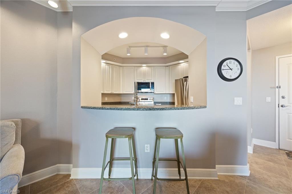 Kitchen featuring stainless steel appliances, white cabinets, dark stone counters, a kitchen bar, and light tile patterned floors