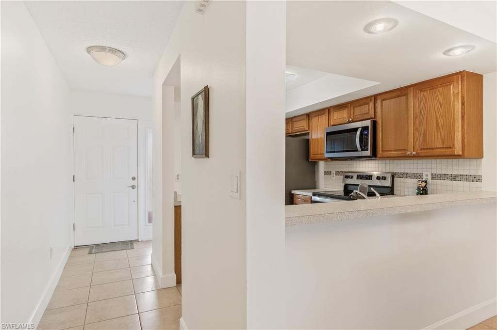 Kitchen featuring backsplash, light tile patterned flooring, light countertops, stainless steel appliances, and brown cabinetry