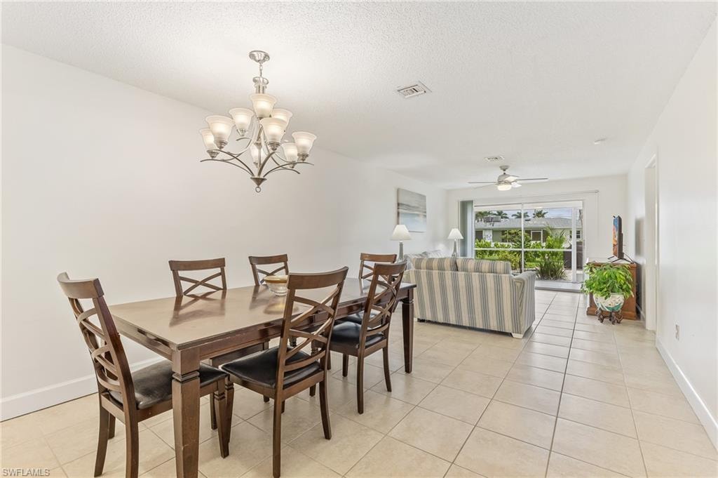 Dining area with light tile patterned floors, a chandelier, ceiling fan, and a textured ceiling