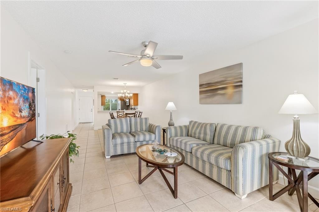 Living area with light tile patterned flooring, a chandelier, a ceiling fan, and a textured ceiling