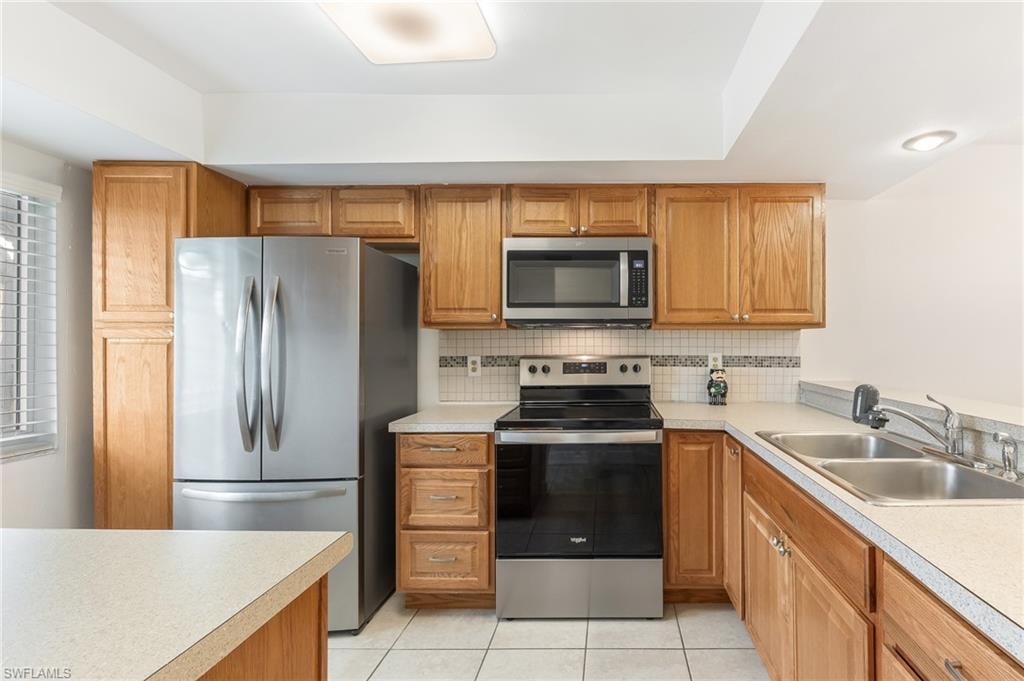 Kitchen with stainless steel appliances, brown cabinets, light countertops, decorative backsplash, and light tile patterned floors