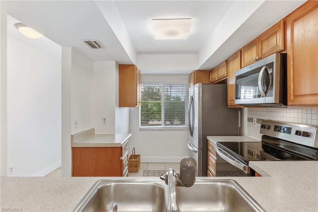 Kitchen featuring appliances with stainless steel finishes, light countertops, light tile patterned flooring, brown cabinets, and tasteful backsplash