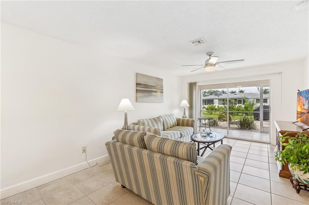Living area with light tile patterned flooring, a ceiling fan, and a textured ceiling