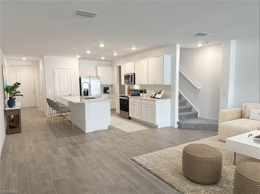 Virtually staged kitchen featuring stainless steel appliances, white cabinets, a kitchen island with sink, recessed lighting, and light wood-style floors