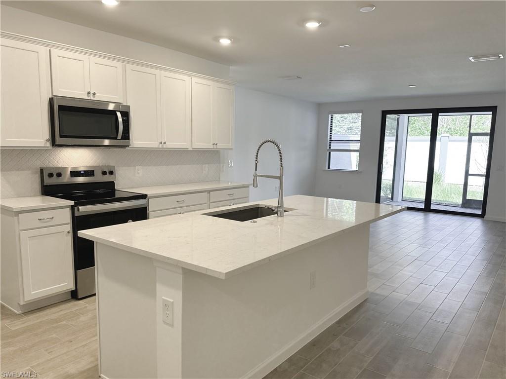 Kitchen with appliances with stainless steel finishes, backsplash, wood tiled floors, light stone countertops, and white cabinetry