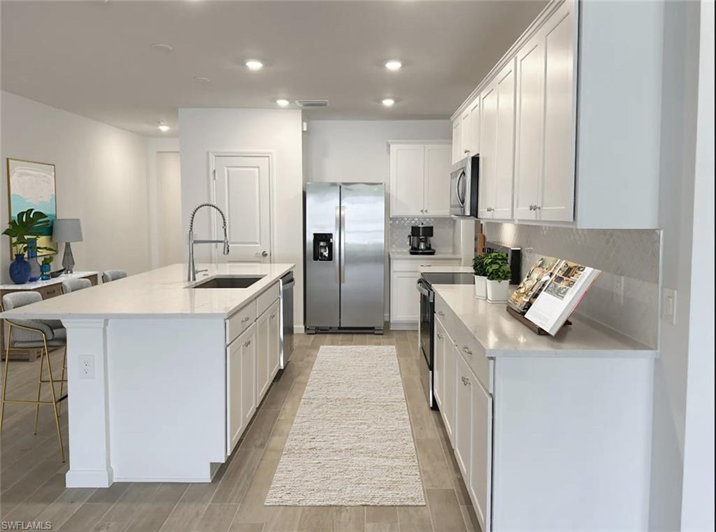 Virtually staged kitchen featuring stainless steel appliances, white cabinetry, light stone countertops, light wood-style flooring, and backsplash