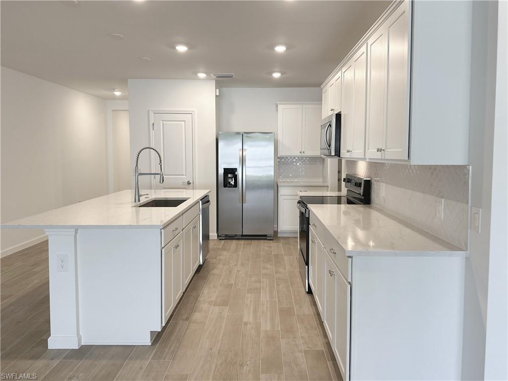 Kitchen featuring stainless steel appliances, white cabinetry, light stone countertops, light wood-style flooring, and backsplash