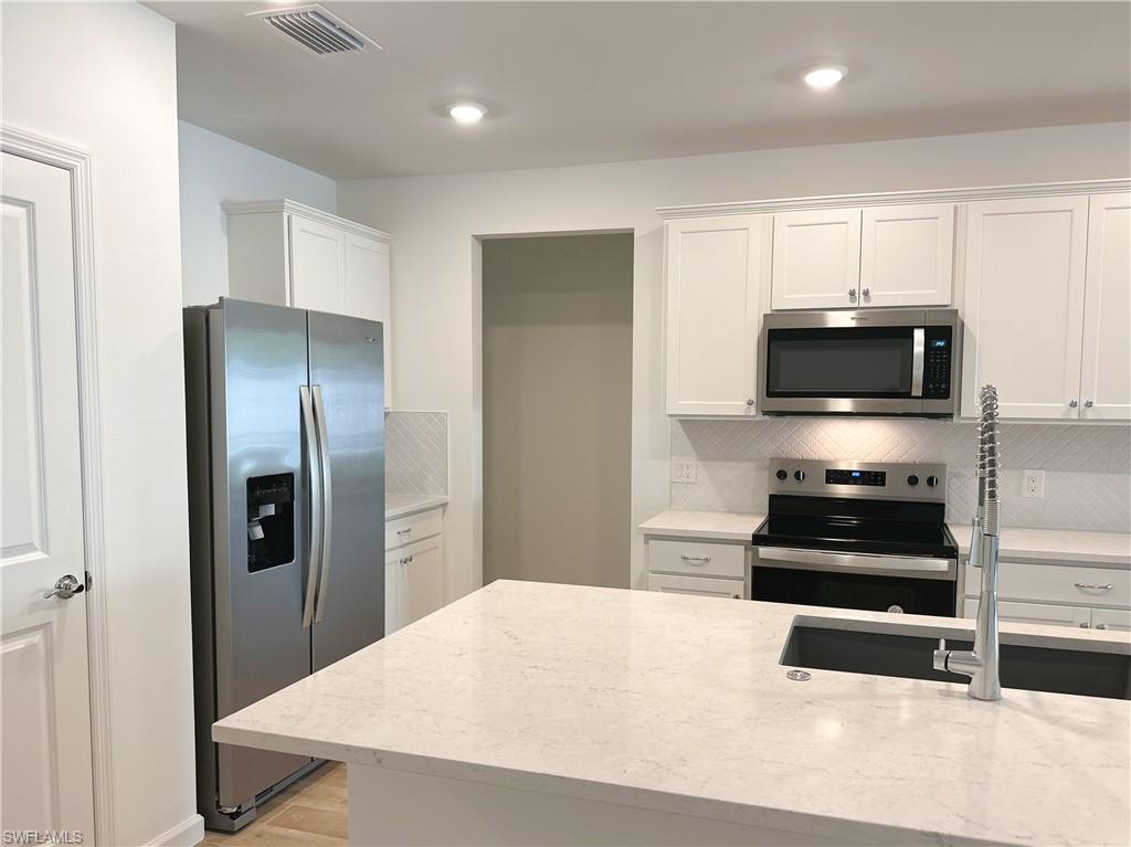 Kitchen with stainless steel appliances, white cabinets, light stone countertops, tasteful backsplash, and light wood-style floors