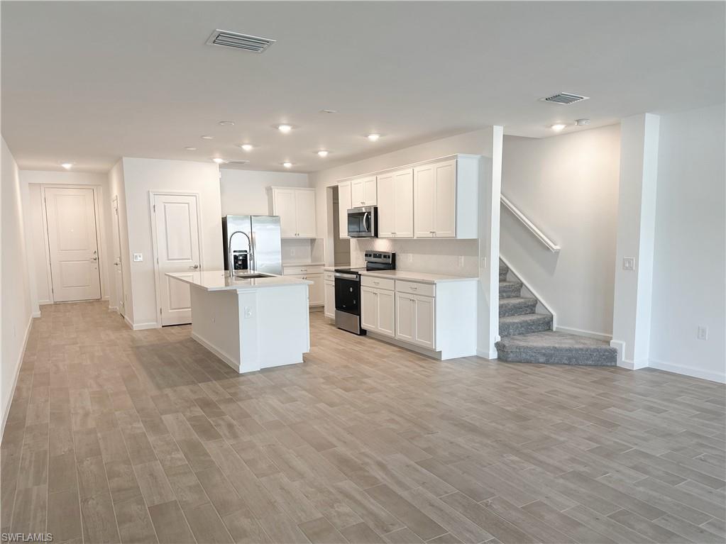 Kitchen featuring stainless steel appliances, white cabinets, a kitchen island with sink, recessed lighting, and light wood-style floors